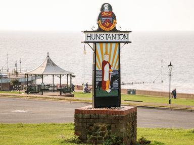 A seaside sign with the word Hunstanton and an illustration of a crowned figure with a dog near a pavilion and the sea in Hunstanton