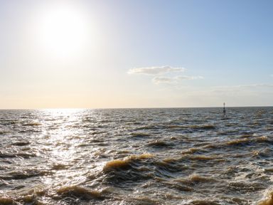 A large body of water with waves under a clear sky and a sun reflecting off the surface at 57 Southend Road in Hunstanton