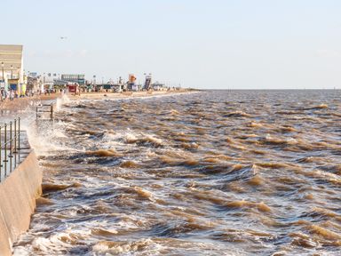 A seafront with waves crashing against a seawall and a promenade with buildings and people at 57 Southend Road in Hunstanton