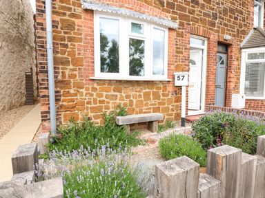 A front garden with plants wooden fence bench and a house with a white door and brick wall at 57 Southend Road Hunstanton