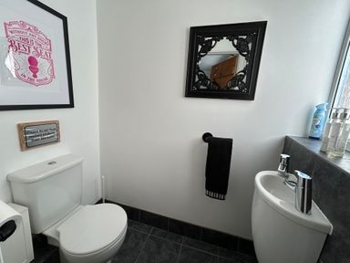 A bathroom with a toilet sink black towel and framed signs at 57 Southend Road Hunstanton