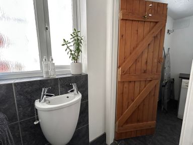 A bathroom with a small white sink under a frosted window and a wooden door leading to an adjacent room at 57 Southend Road in Hunstanton