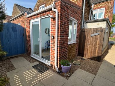 An exterior corner of a brick house with glass sliding doors and a wooden gate labeled bin store 57 Southend Road Hunstanton