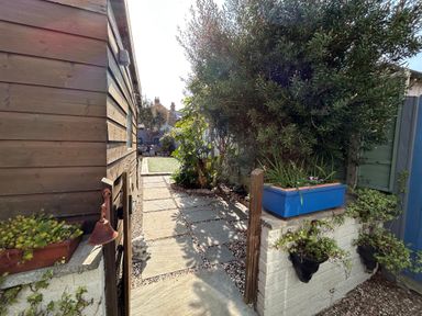 A garden path with stone tiles and plants along the sides near a wooden shed at 57 Southend Road in Hunstanton