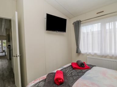 A bedroom with a bed covered with towels and a wall-mounted television at Happy Daze in Carnaby near Bridlington