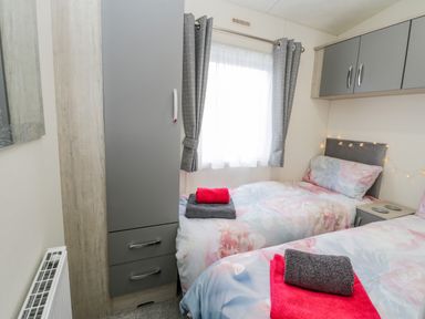 A bedroom with two single beds grey curtains and grey cabinets at Happy Daze Carnaby near Bridlington