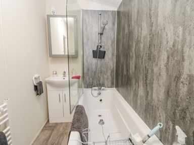A bathroom with a bathtub shower combination a sink cabinet and a towel rail at Happy Daze in Carnaby near Bridlington