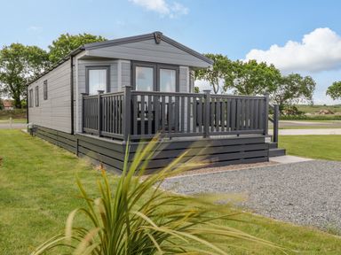 A small grey mobile home with a porch and railing on grass at Happy Daze in Carnaby near Bridlington