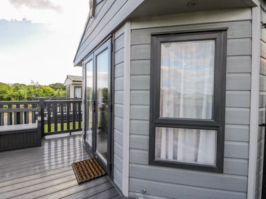 A deck with railing a doormat glass doors and a window on a grey wooden house at Happy Daze Carnaby near Bridlington