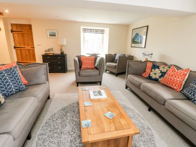 A living room with gray sofas and armchairs around a wooden coffee table at 8 Llwyn Onn in Llanfairpwllgwyngyll