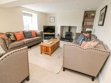 A living room with two beige sofas a wooden coffee table a wood burning stove and a bookshelf at 8 Llwyn Onn in Llanfairpwllgwyngyll