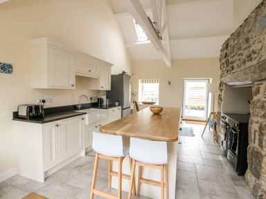 A kitchen with a wooden island and two white chairs near a stone wall at 8 Llwyn Onn in Llanfairpwllgwyngyll
