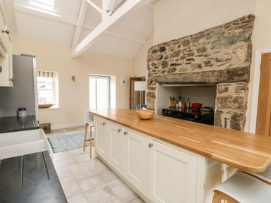 A kitchen with a wooden countertop island stone fireplace and stools at 8 Llwyn Onn in Llanfairpwllgwyngyll