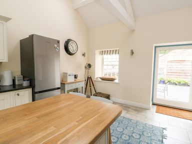 A kitchen with a stainless steel refrigerator wooden countertop table clock on the wall and a door leading outside at 8 Llwyn Onn in Llanfairpwllgwyngyll