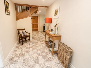 A hallway with patterned tile floor a wooden chair with a cushion a wooden console table with a lamp and books and a wicker basket at 8 Llwyn Onn in Llanfairpwllgwyngyll