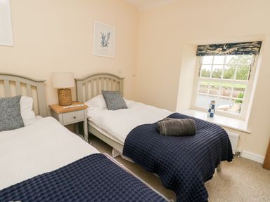 A bedroom with two single beds a nightstand with a lamp a window with a decorative blind and a small lighthouse ornament at 8 Llwyn Onn in Llanfairpwllgwyngyll