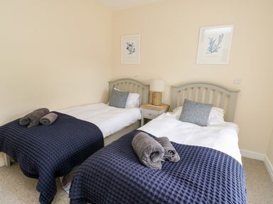 A bedroom with two single beds with blue blankets and gray pillows and a nightstand with a lamp between them at 8 Llwyn Onn in Llanfairpwllgwyngyll