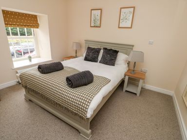 A bedroom with a double bed two bedside tables with lamps and a window with a patterned blind at 8 Llwyn Onn in Llanfairpwllgwyngyll