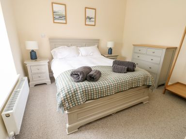 A bedroom with a double bed two bedside tables two lamps a chest of drawers and a coat rack at 8 Llwyn Onn in Llanfairpwllgwyngyll
