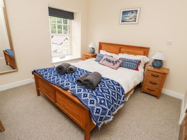 A bedroom with a wooden bed with blue patterned blankets and pillows two bedside tables with lamps and a window with a black blind at 8 Llwyn Onn in Llanfairpwllgwyngyll