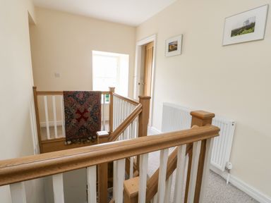 A staircase landing with wooden banisters a window a wall radiator and framed pictures at 8 Llwyn Onn in Llanfairpwllgwyngyll
