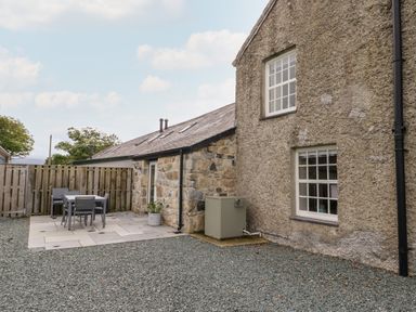 An outdoor patio area with a table and chairs next to a stone and plaster building at 8 Llwyn Onn in Llanfairpwllgwyngyll