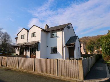 A two-story white house with a wooden fence and a small patio with chairs at Aran in Beddgelert