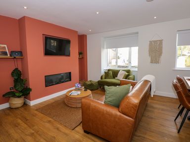 A living room with a brown leather sofa green armchair coffee table and wall mounted TV at Aran in Beddgelert