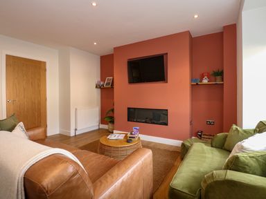 A living room with a wall-mounted television above a fireplace and green and brown sofas at Aran in Beddgelert