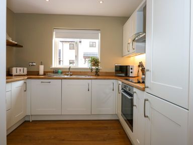 A kitchen with white cabinets wooden countertops a microwave a toaster and a window at Aran in Beddgelert