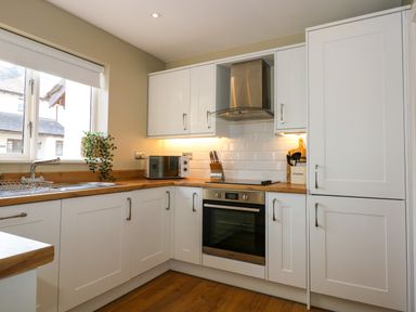 A kitchen with white cabinets a wooden countertop oven microwave and a window at Aran in Beddgelert