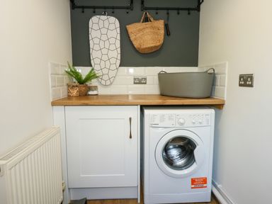 A laundry room with a washing machine a cabinet wooden countertop ironing board basket and plants at Aran in Beddgelert