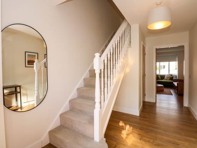 A hallway with carpeted stairs and wooden floor with a mirror on the left wall leading to a living room at Aran in Beddgelert