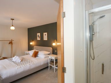 A bedroom with a double bed two nightstands and a shower visible through an open door at Aran in Beddgelert