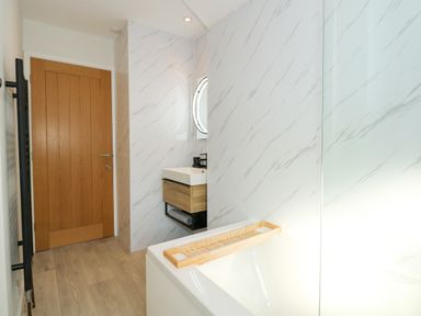 A bathroom with a wooden door a bathtub with a wooden tray a floating sink with a mirror and marble patterned walls at Aran in Beddgelert