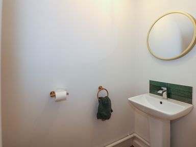 A bathroom with a pedestal sink a round mirror above and a towel ring with a dark towel at Aran in Beddgelert