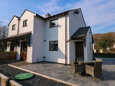 A white two story house with outdoor patio and wicker chairs around a glass table at Aran in Beddgelert