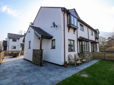 Exterior view of a white two-story house with brown window frames and a tiled patio with chairs at Aran in Beddgelert
