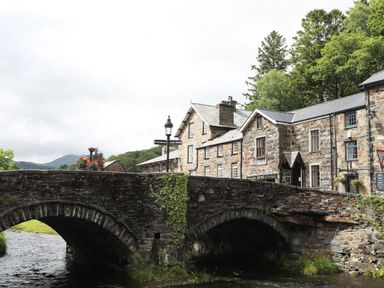 A stone bridge over a river with stone buildings and trees in the background at Aran in Beddgelert