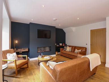 A living room with brown leather sofas a wooden rocking chair a mounted television and a modern fireplace at Craig y Llan in Beddgelert