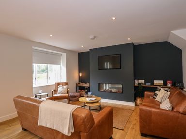 A living room with brown leather sofas a chair a wall-mounted TV and a built-in fireplace at Craig y Llan in Beddgelert