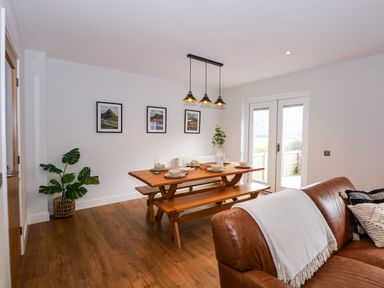 A dining area with a wooden table and benches set with plates and glasses next to a brown leather sofa at Craig y Llan in Beddgelert