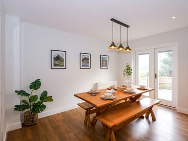 A dining area with a wooden table and benches set with plates and glasses near glass doors at Craig y Llan in Beddgelert