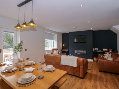 A dining table set with dishes and glassware next to a living room with brown leather sofas and a wall-mounted TV at Craig y Llan in Beddgelert