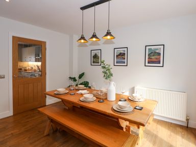 A dining room with a wooden table set for six people and three framed pictures on the wall at Craig y Llan in Beddgelert
