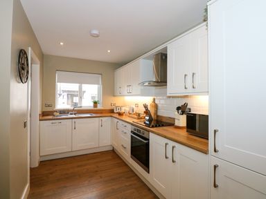 A kitchen with white cabinets wooden countertops a built-in oven and a window at Craig y Llan in Beddgelert