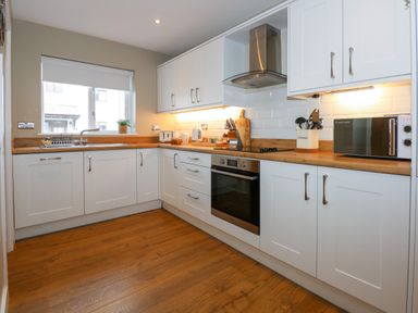 A kitchen with white cabinets wooden countertops a window and various appliances at Craig y Llan in Beddgelert