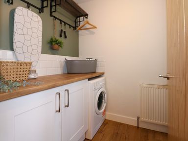 A laundry room with a washing machine under a wooden countertop and an ironing board on the wall at Craig y Llan in Beddgelert