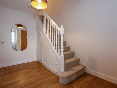 A carpeted staircase with white banisters and a wooden floor with a wall mirror and ceiling light at Craig y Llan in Beddgelert