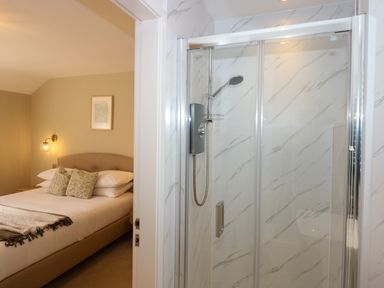 A bedroom with a bed and pillows next to a bathroom with a glass shower at Craig y Llan in Beddgelert